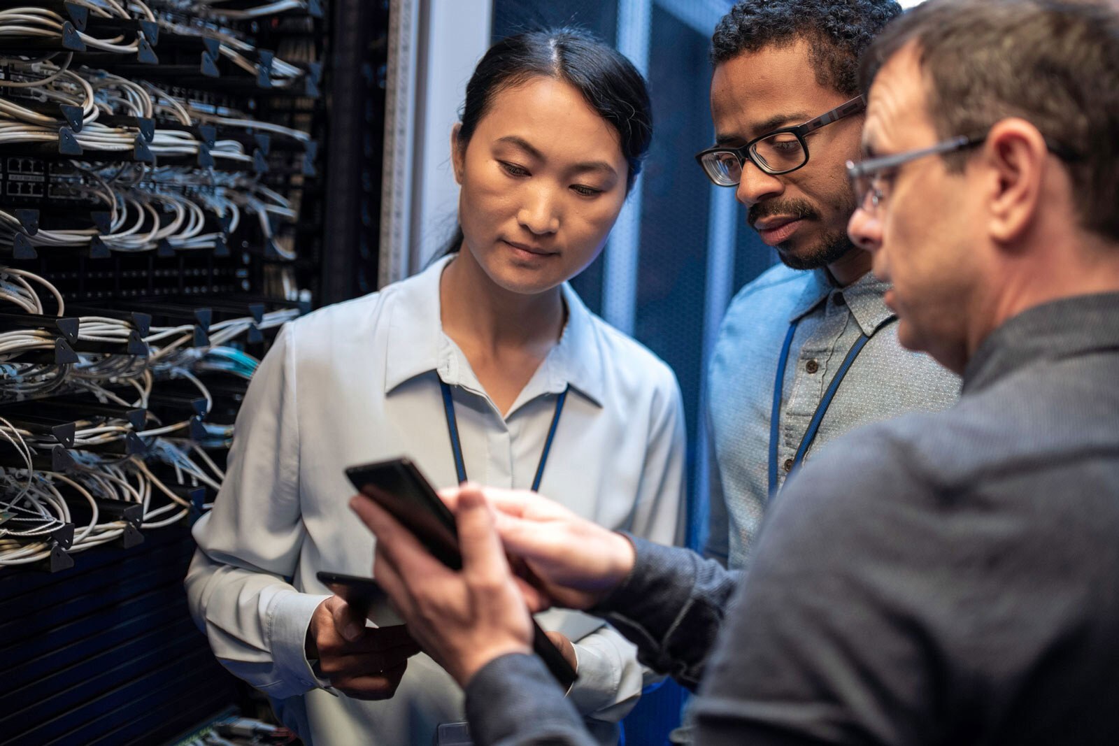 Three employees in server room looking at a tablet and discussing